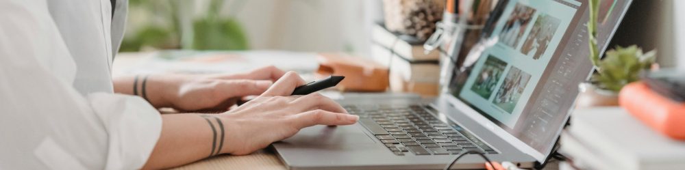 Freelance designer working from home using a laptop and digital tablet, surrounded by plants.
